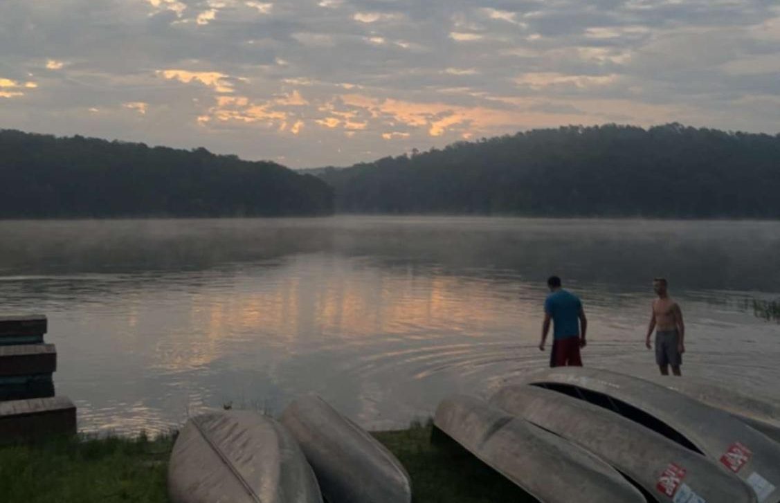 Counselors Will Schuering and Adrian Sabeh watch the sunrise while wading in the lake.